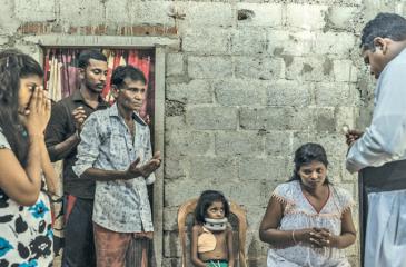 A priest prays with the family of a seven-year-old victim of a bomb blast