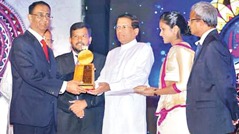 President Sirisena presents an award to a winner. Minister of Industry and Commerce Rishad Bathiudeen looks on.