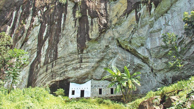Massive rock of Batadombalena cave, a home of ‘Balangoda Man’,  a clump of banana trees in the   foreground of the cave
