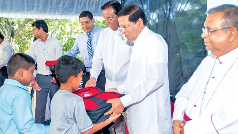 President Maithripala Sirisena presents books and bags to students. Auxiliary Bishop of Colombo Emmanuel Fernando, Minister John Amaratunga and Dinesh Weerakkody are also in the picture.
