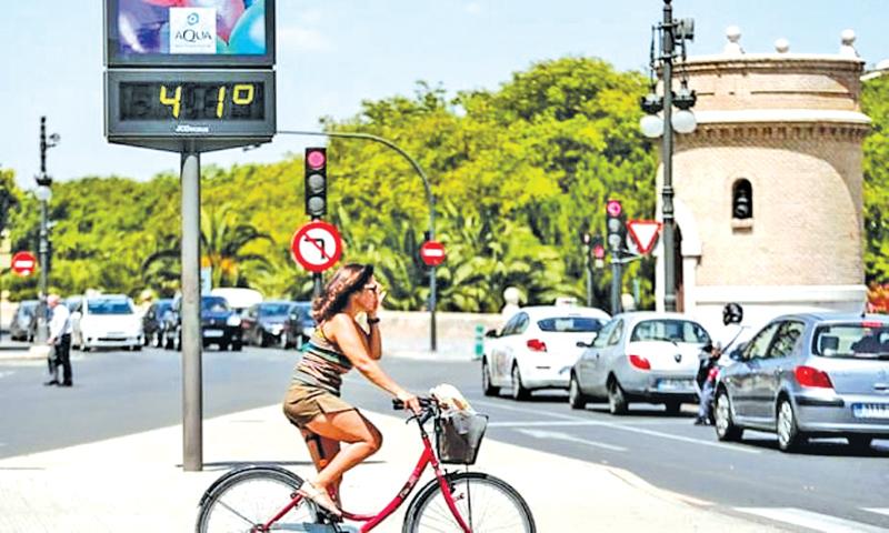 A cyclist waits to cross a road next to a thermometer showing 41C in Valencia, eastern Spain.  Pic: Manuel Bruque/EPA    