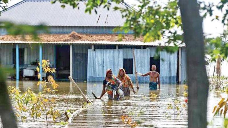 Women with goats come out of their submerged house, in Shibaloy, Manikganj district, Bangladesh. Credit: Farid Ahmed/IPS