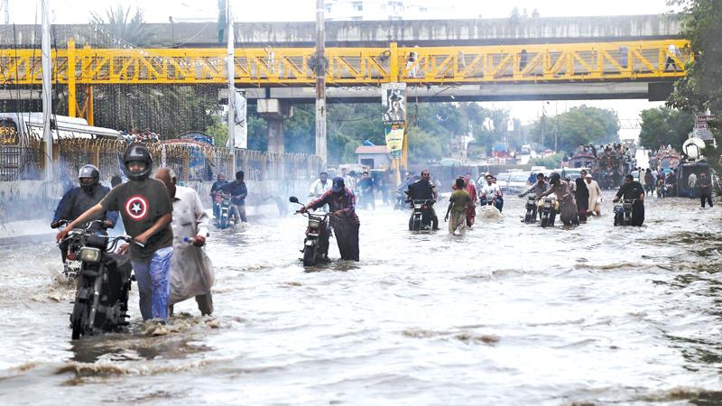Pic: Rehan Khan/EPA People make their way through flooded streets after a heavy downpour in Karachi  on Thursday.