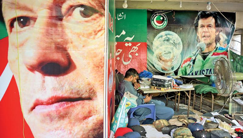A vendor sits at his stall beside the posters of Pakistan’s cricketer-turned politician Imran Khan                        (AFP)
