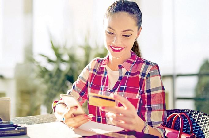 Girl is shopping online using her mobile phone and credit card in a cafe