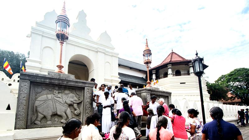 THE MAJESTIC GUARDIANS: Pilgrims enter the Sri Dalada Maligawa near the stone walls of the temple which bear bas-relief testament to the  elephants’ centuries of service   