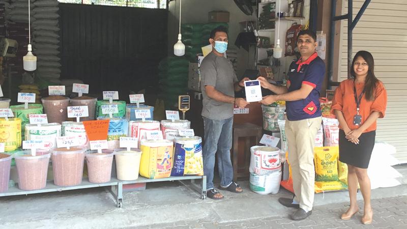 Manager, Merchant Acquiring, DFCC Bank, Chrishan Jayamanne (in the middle) presents a QR Code, POS material to a merchant at the Narahenpita Economic Centre during the promotional campaign.