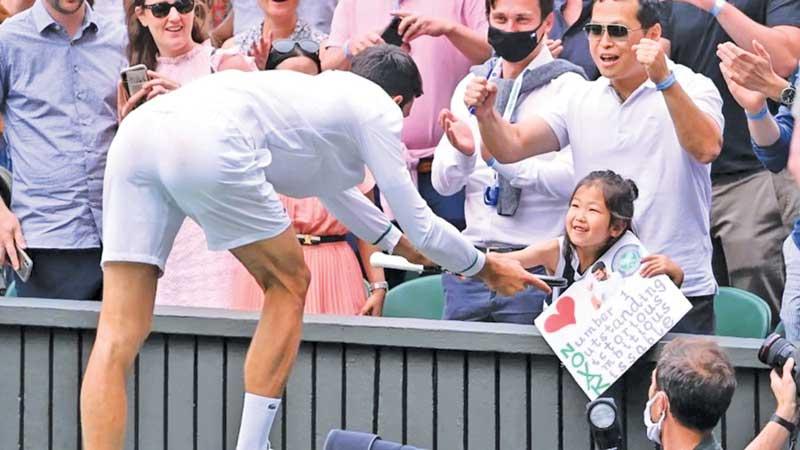 Novak Djokovic presents his racket to a young fan in the front row after his win at Wimbledon 2021