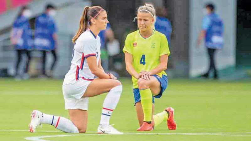 Women’s football players from Sweden and the US take a knee bow before the start of their match at the Tokyo Olympics