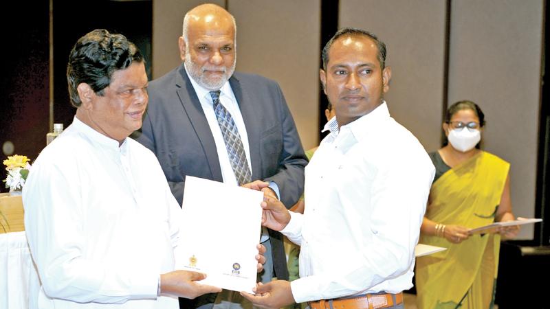 Trade Minister Bandula Gunawardhana presents a certificate to an exporter. EDB Chairman Suresh De Mel and officials look on.