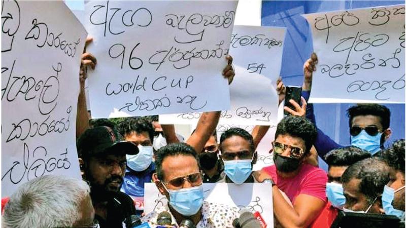 Protesters carry a banner questioning the logic behind the ouster of Bhanuka Rajapakse from the team