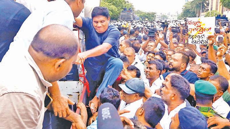 Opposition leader Sajith Premadasa making a desperate attempt to climb on to a vehicle stage supported by parliamentarians Dayasiri Jayasekera and Chandima Weerakody. pic Sulochana Gamage