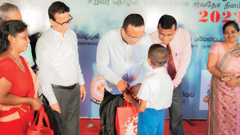 Minister Manusha Nanayakkara presents a gift to a child. Maliban Biscuit Manufactory and Labour Department officials look on.