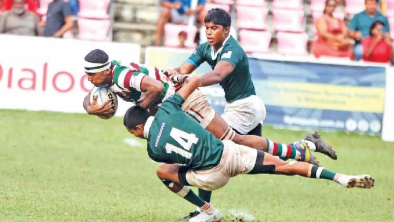 Two Isipathana College players Rinesh Silva (14) and skipper Naveen Kanishka grapple to bring down Zahira College’s Number Eight Aadil Rafeek (Pic by Thilak Perera)